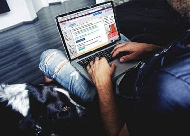 A man reads email on his laptop beside a dog. / digital nomad / remote worker / mobile computing